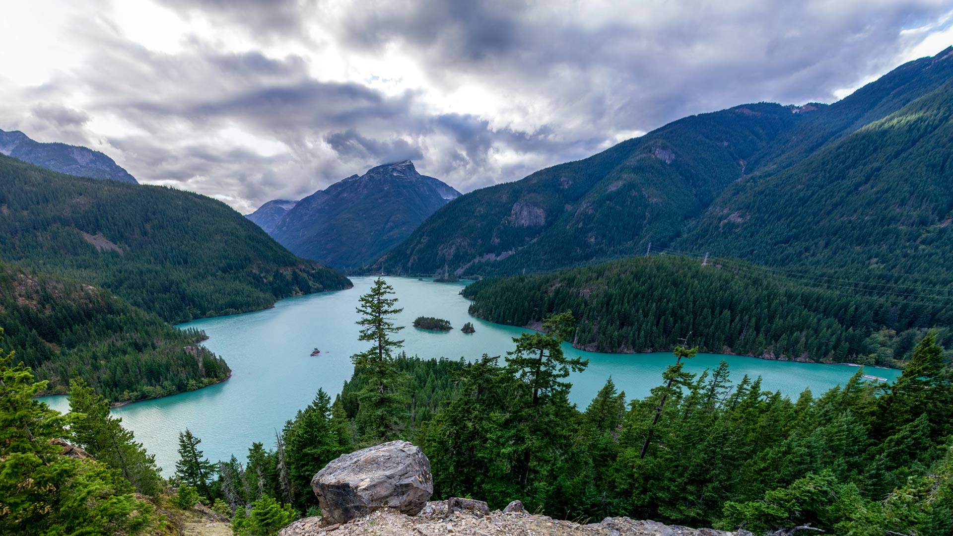 Landscape image of green mountains with a blue lake below it on a cloudy day.