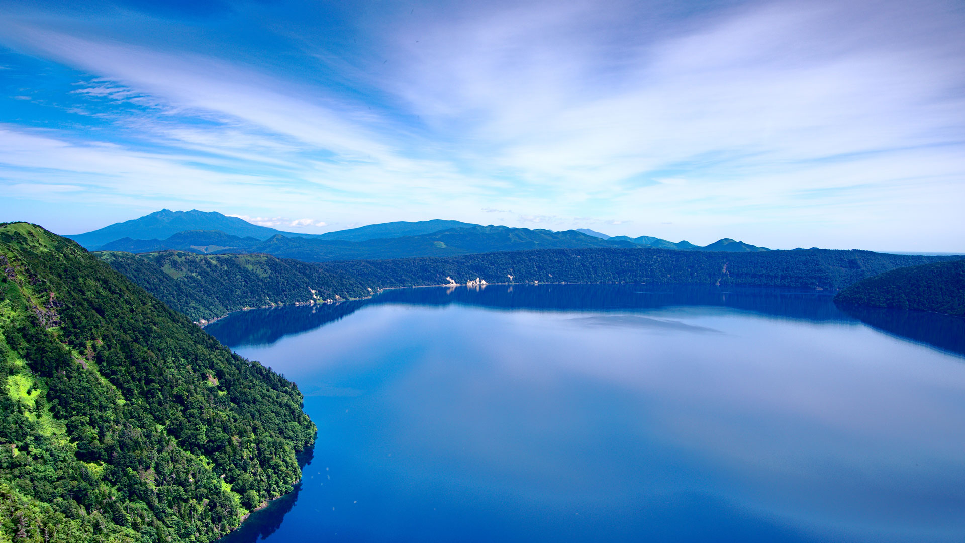 Landscape image of vivid blue sky with deep blue scenary of a lake surrounded by green terrain.